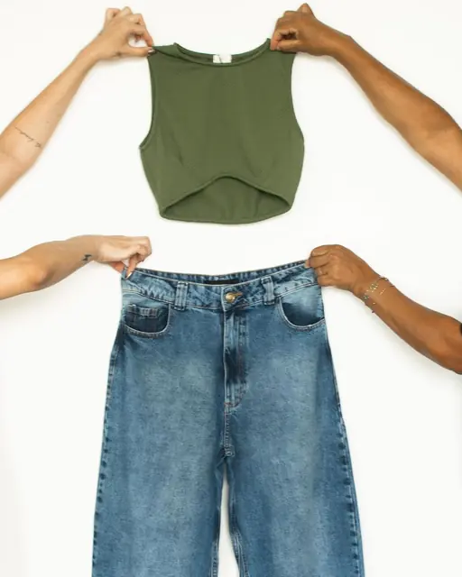 Cropped verde e calça jeans segurados por mãos sobre fundo branco, foto de produto