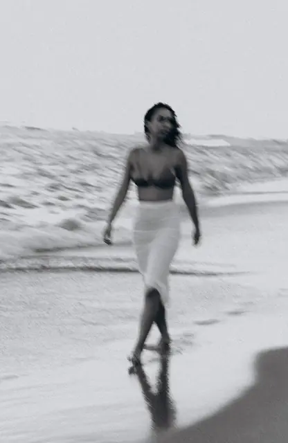 Mulher caminhando na beira do mar, em preto e branco