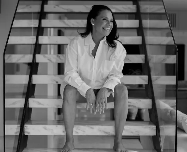 Mulher de camisa branca sentada numa escada, em preto e branco