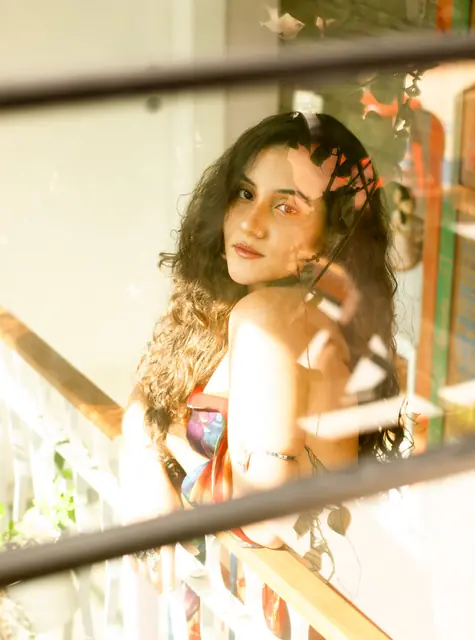 Mulher de cabelo cacheado apoiada num corrimão, olhando por cima do ombro, luz quente